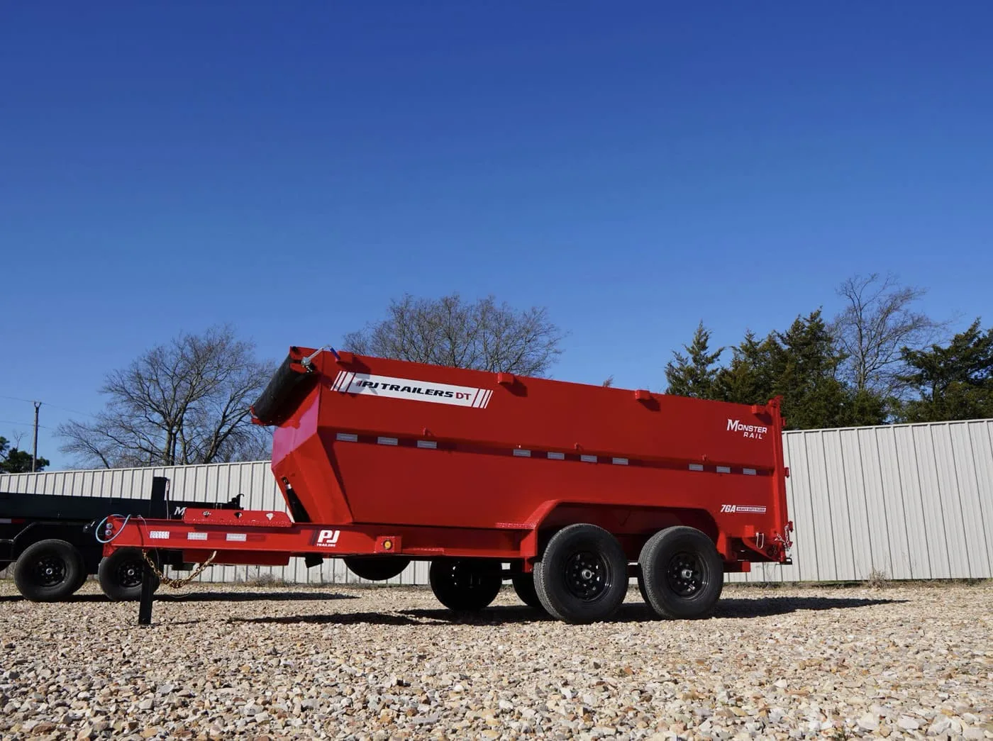 Profile of a red High-side PJ Dump Trailer in front of a white fence