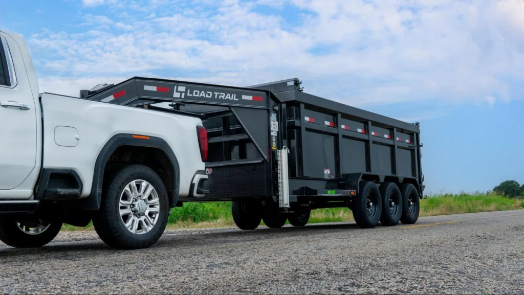 Load Trail Gooseneck Dump Trailer hooked up to a white pick up truck driving on a gravel road