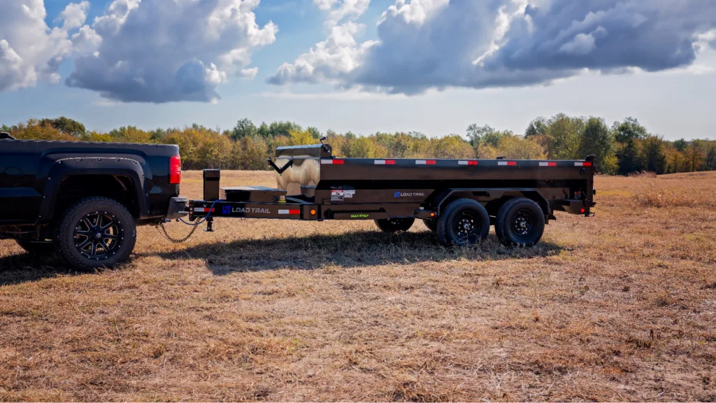 Black 7x12 Load Trail Dump Trailer in a Field hooked up to a black truck