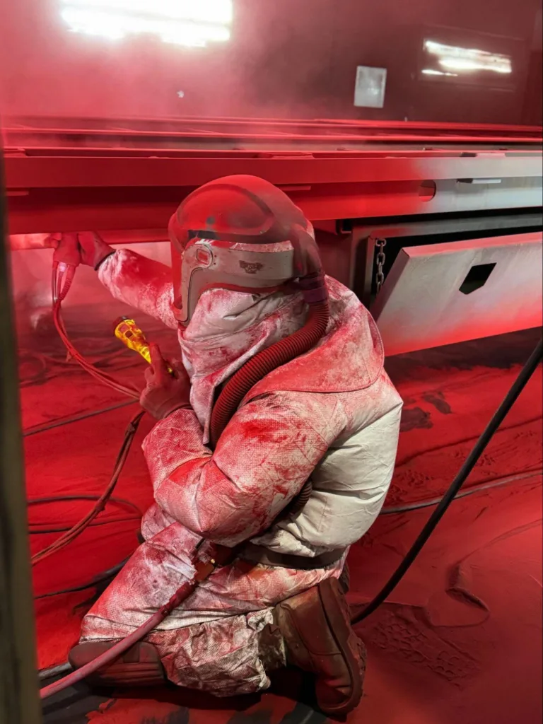 Person in coveralls holding a flashlight and paint run powdercoating a trailer red